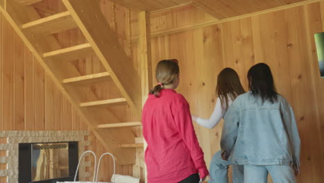 women drop there bags on wooden bench inside cabin kitchen near window, sunlight illuminating rustic walls, purses and duffel in hand as they prepare to leave room and climb staircase