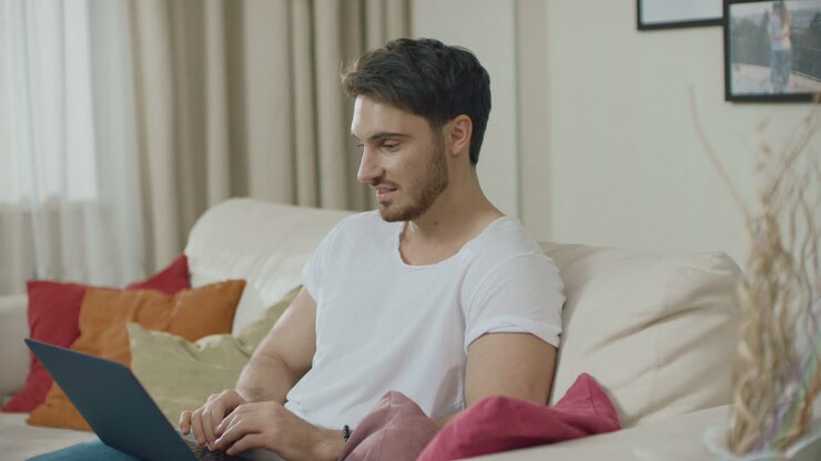 Smilende mand arbejder med bærbar computer på sofa derhjemme