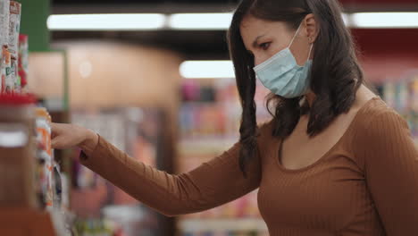 a woman shopping and picking up groceries in a supermarket in a protective mask during an epidemic