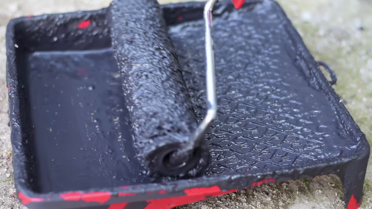 Close up of a roller brush picking up black dye on from a red paint roller tray
