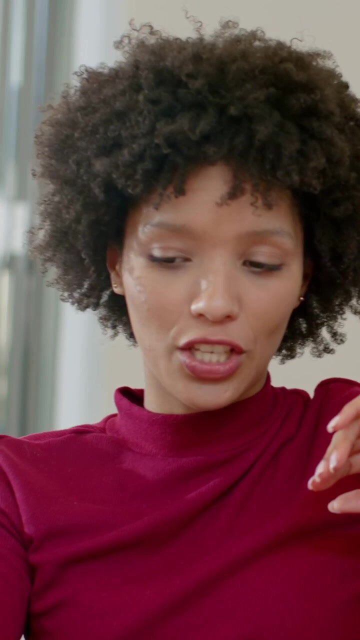 Vertical video: Talking woman in maroon top reacting to friend's hand gesturing, listening on sofa
