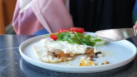 persona que come un desayuno de huevos fritos con hongos y verduras