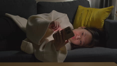 woman spending evening at home lying on sofa with mobile phone scrolling through internet or social media 10