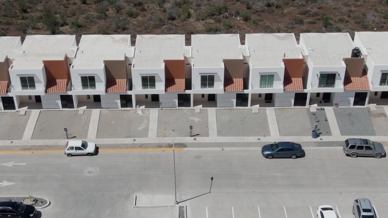 Luftfoto fra drone af moderne beboelseshuse langs en brolagt bygade med parkerede køretøjer og et voksende kvarterslandskab