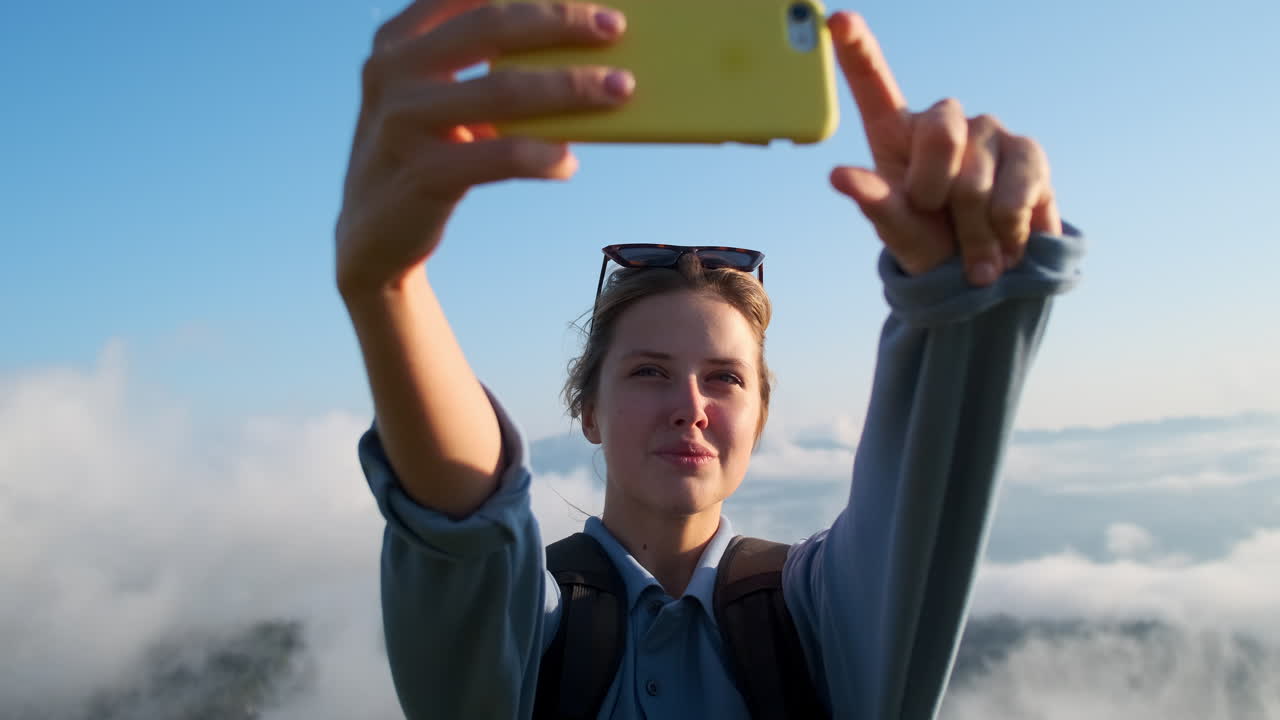 mujer tomando una selfie en la cima de una montaña por encima de las nubes