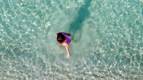 Una-Mujer-En-Traje-De-Baño-Rosa-Disfruta-Haciendo-Círculos-En-El-Mar-Turquesa,-Capturada-En-Una-Vista-Aérea-De-Arriba-Hacia-Abajo