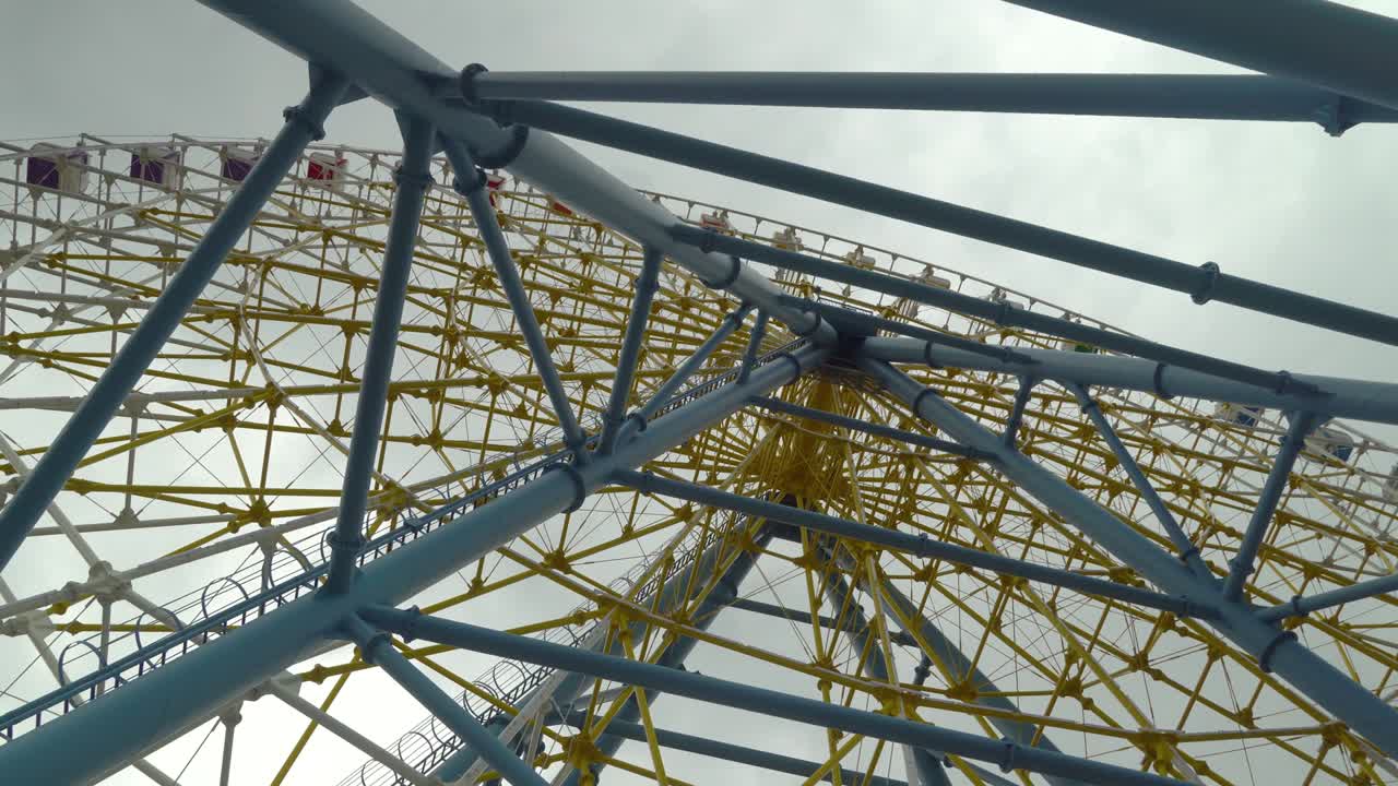 Ferris wheel shot against the clouds and overcast sky. Warm colors, daylight.