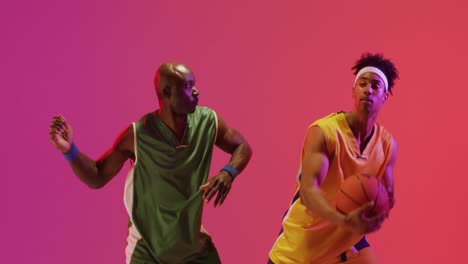 video of two diverse male basketball players facing playing with ball on pink background