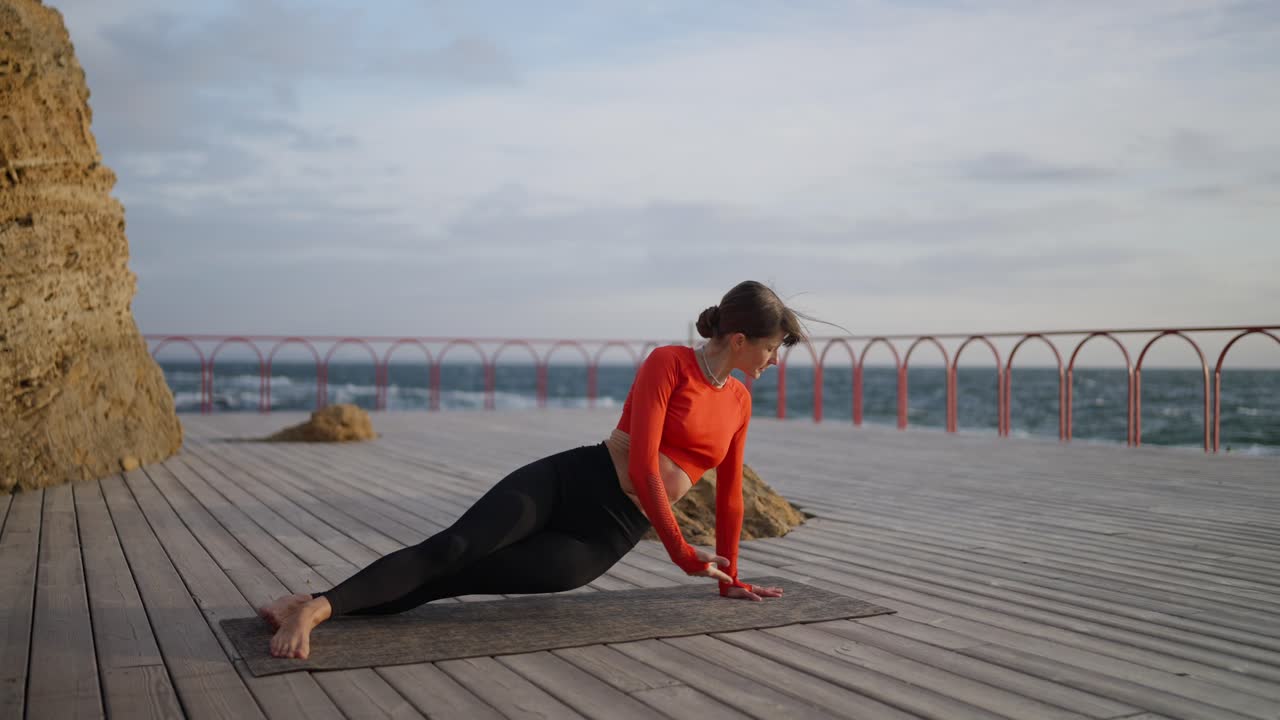 mujer practicando yoga en una cubierta de madera junto al océano