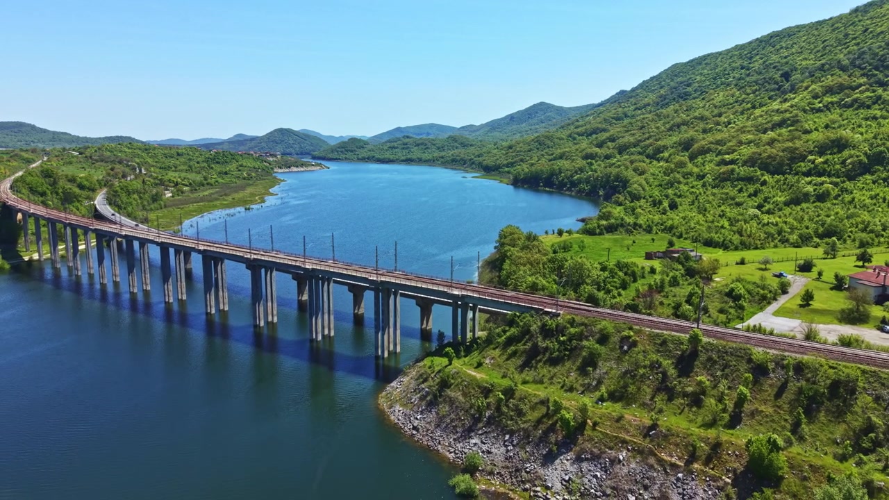 Ponte Ferroviario che Attraversa un Grande Fiume con Colline Verdi sullo Sfondo Durante una Giornata di Sole Splendente in un'Area Rurale