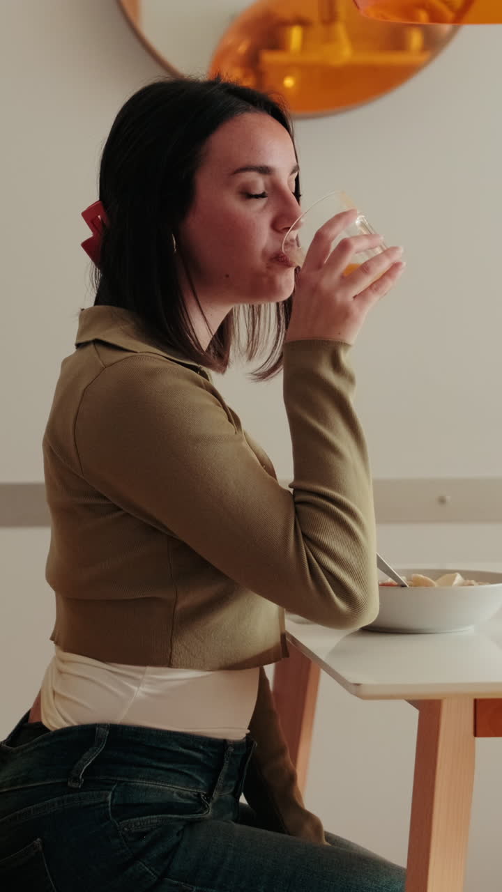 Side view of Young Woman Drinking Orange Juice in Kitchen