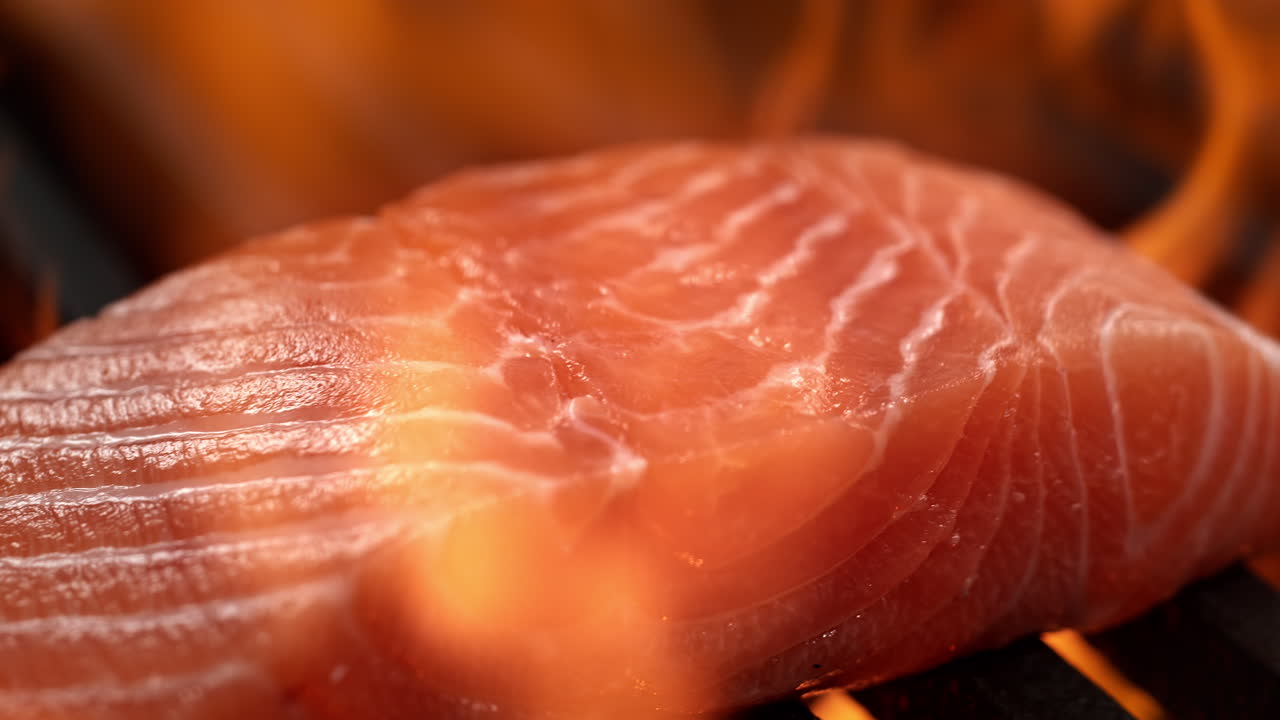 filete de salmón crudo parrilla en la parrilla de carbón entre llamas estallantes, barbacoa en macro y cámara lenta