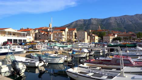 Hafen-Und-Boote-Auf-Der-Kroatischen-Insel-Im-Adriatischen-Meer,-Mittelalterliche-Häuser-Und-Berge-Im-Hintergrund,-Kroatien