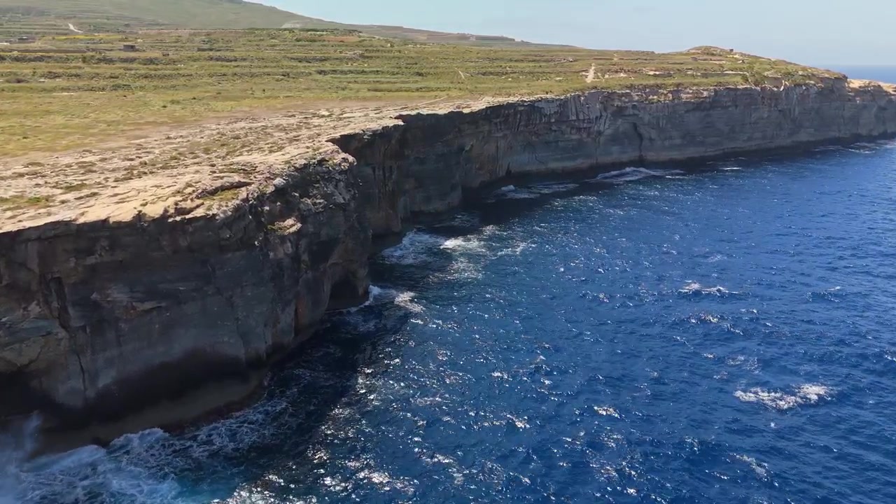 Wied il-Għasri a Gozo, Malta, con scogliere costiere rocciose, acqua azzurra e limpida e onde lungo la costa mediterranea, catturato in estate da una vista panoramica con drone.