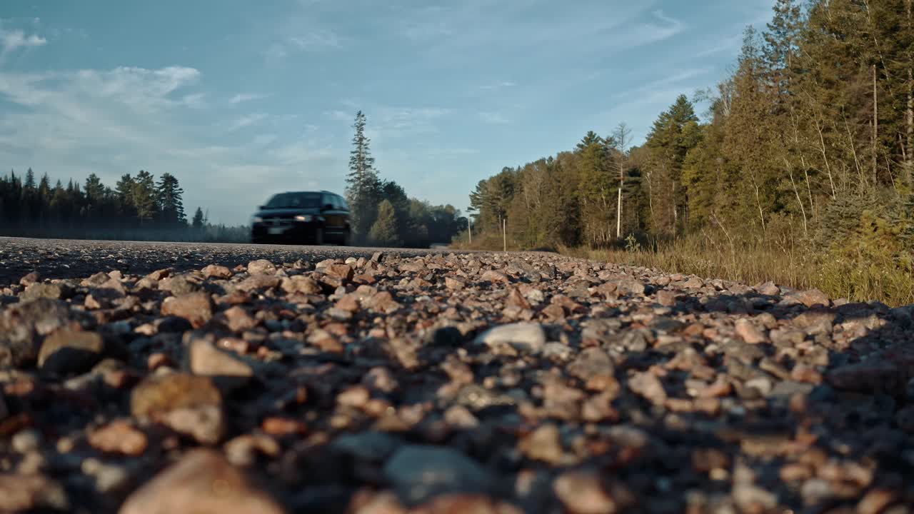 Ground level shot of minivan driving down rural Ontario highway toward camera on gravel shoulder