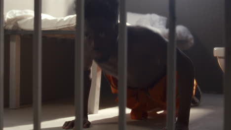 strong black inmate practicing pushups during workout in prison cell