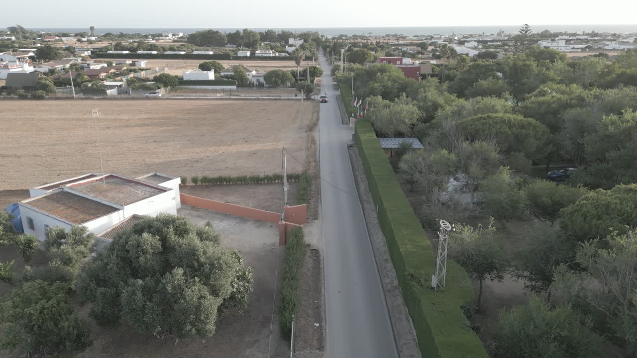 Ripresa con drone che sorvola una strada di campagna verso il mare in Spagna al tramonto.