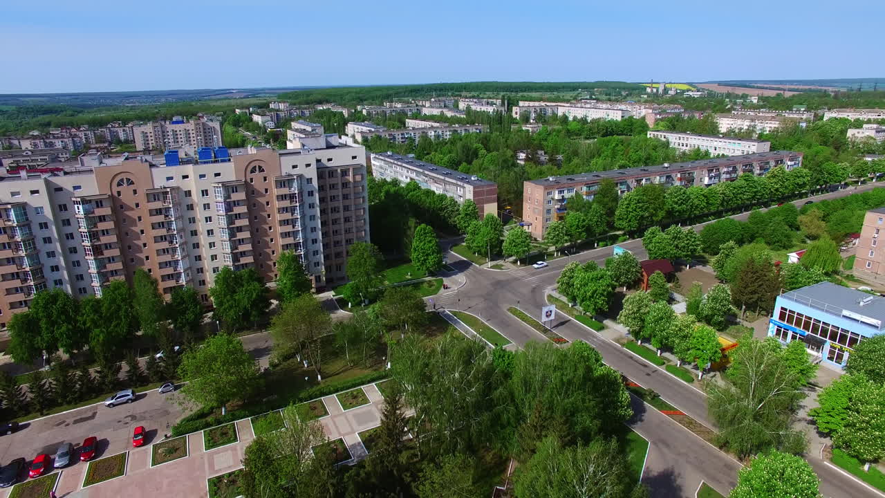 Provincial city panorama on sunny summer daytime. Drone footage over the multi-storied buildings, roads and city square. Top view.