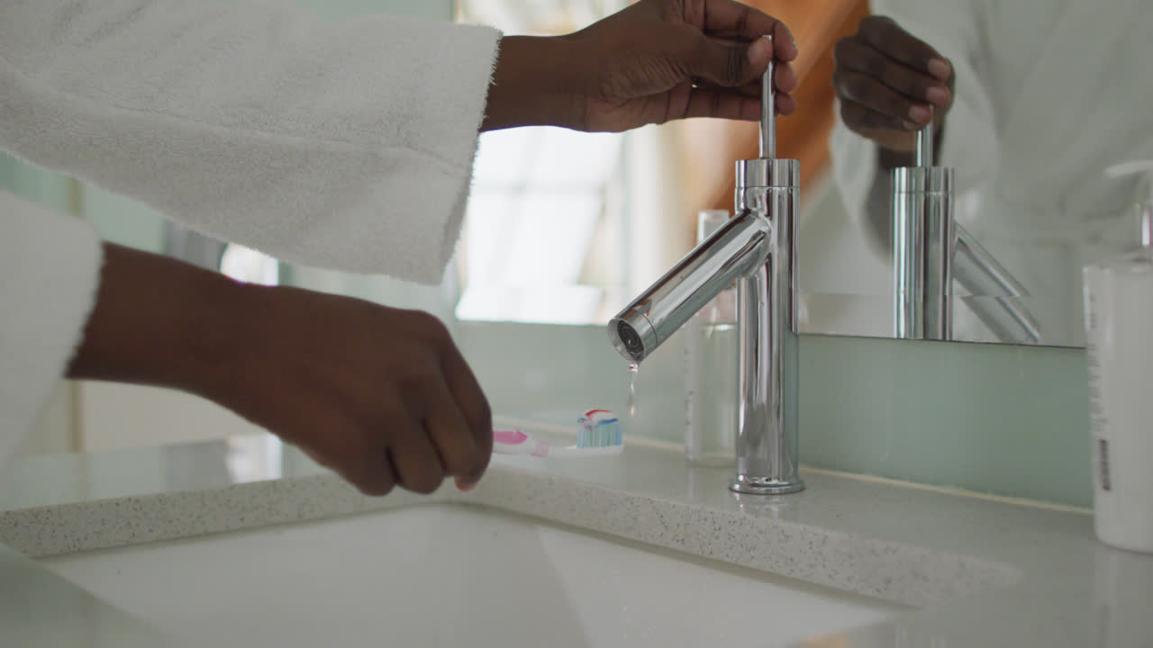 Mani di un'attraente donna afroamericana che applica il dentifricio sullo spazzolino in bagno.