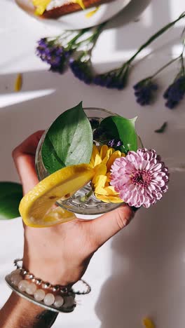 hand holding a glass with flowers and lemon