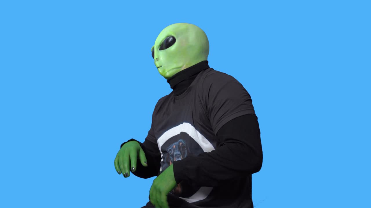 Professional artist in alien costume and in a black t-shirt laughs and clutches his head in hysteria against blue chromakey background. Role rehearsal