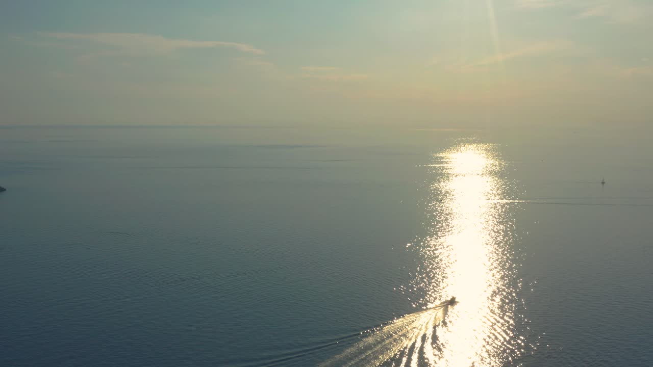 Rising aerial shot following a boat that rides the waves towards an amazing sun glitter