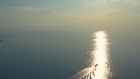 rising aerial shot following a boat that rides the waves towards an amazing sun glitter