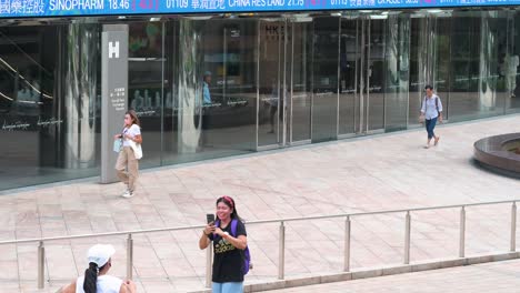 people are busy taking pictures as a moving screen in the background highlights negative stock ticker symbols at exchange square, the site of the hong kong stock exchange in the financial district.