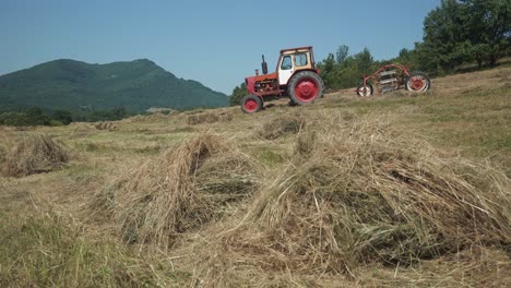 old red tractor and threshing machine in golden hayfield in bulgarian rural countryside meadow