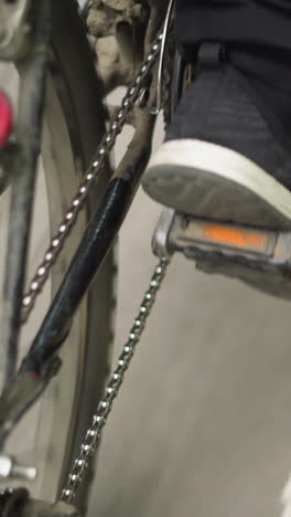 vista trasera de cerca de alguien con pantalones negros y zapatillas de deporte pedaleando una bicicleta en una carretera lisa y asfaltada, se pueden ver marcas de carriles blancos junto con hojas esparcidas en el suelo