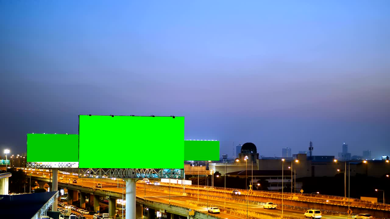 Grøn skærm på reklameskilt på motorvej i skumringen med bybaggrund i Bangkok, Thailand.