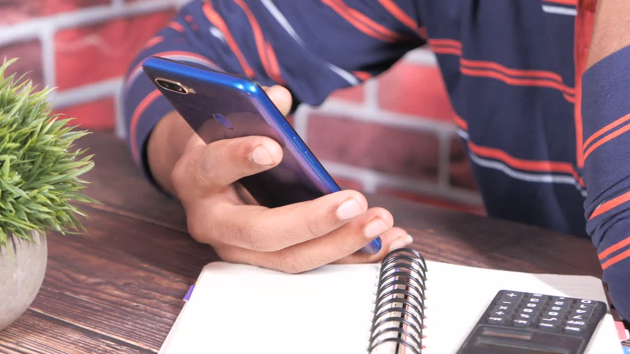 persona que utiliza un teléfono inteligente en un escritorio con un cuaderno y una calculadora