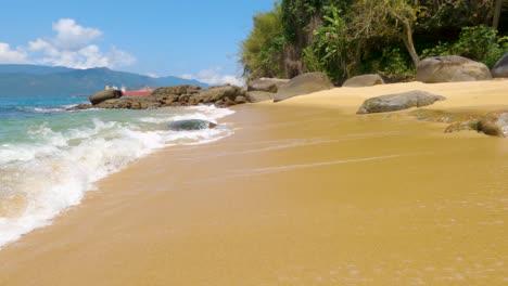 Spazieren-Am-Schönen-Strand-Von-Maciéis-Mit-Meereswellen,-Die-Sich-Auf-Dem-Strandsand-Mit-Felsen-Im-Hintergrund-Brechen---Angra-Dos-Reis