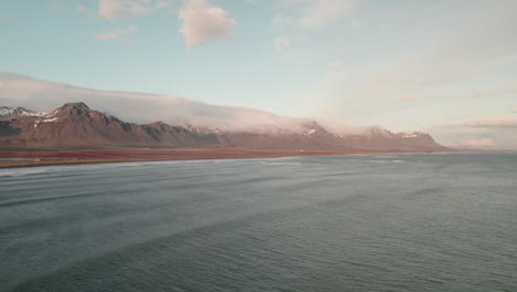 aerial view over ocean looking towards dramatic mountains on iceland shoreline