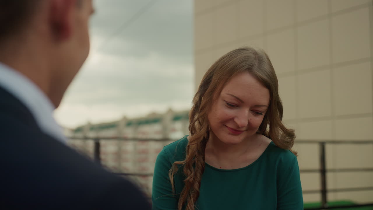caucasian couple rooftop date with champagne. businessman offers toast in opening frame woman in green dress smiles as friend and romantic partner in second frame shy laugh captured during intimate