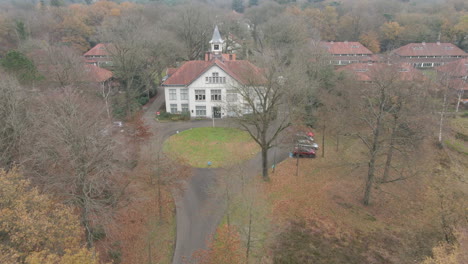 luftaufnahme eines alten herrenhauses mit uhrturm am ende einer ruhigen straße im herbstwald