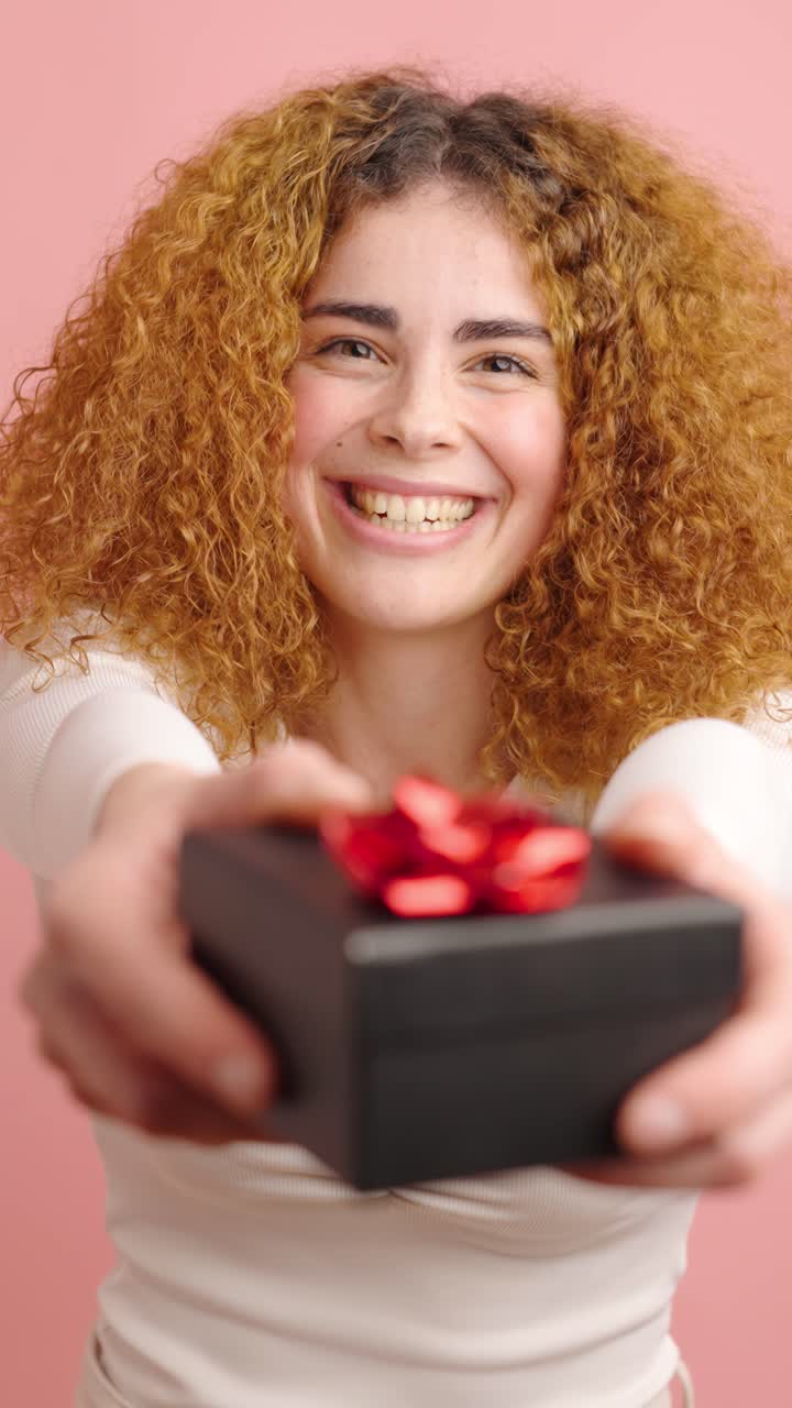 Happy woman giving a gift on pink background
