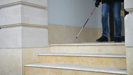 vista lateral de un ciego irreconocible sosteniendo un bastón y saliendo de un edificio mientras baja las escaleras