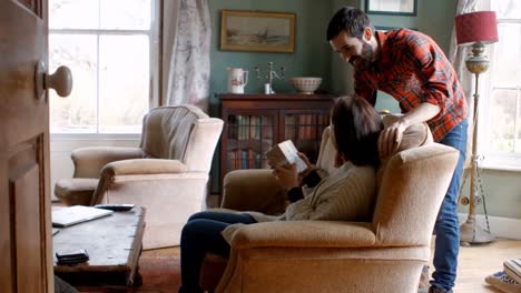 man surprising woman with a gift in living room