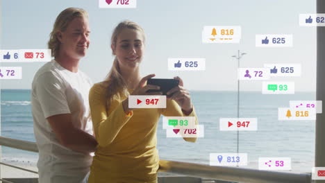 social media notifications animation over people taking selfie by ocean