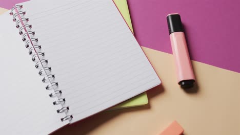 close up of open notebook with school stationery on beige and purple background, in slow motion