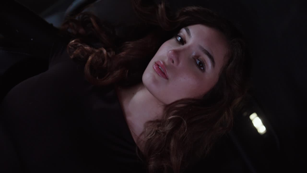 Cinematic close-up of a glamorous woman reclining in the back seat of an SUV at night, looking calm and confident in low light. Concept for luxury ride, nightlife, modern lifestyle, and sensual mood