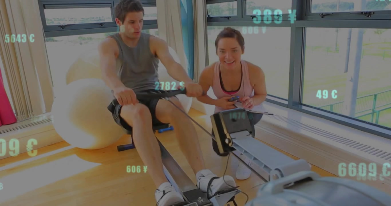 Trainer entering gym timing trainee on rower using stopwatch for form feedback then rowing together