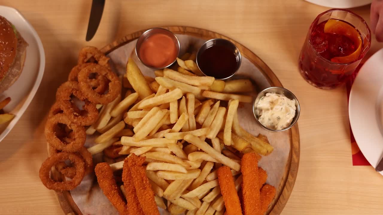 amigos compartiendo una comida de papas fritas, anillos de cebolla y palitos de pescado en un restaurante.