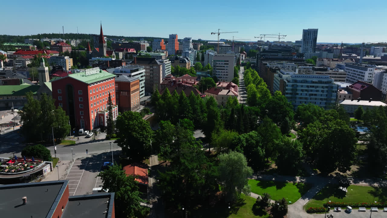 Aerial view of a European city with a mix of modern and historic buildings and a large park under a clear blue sky