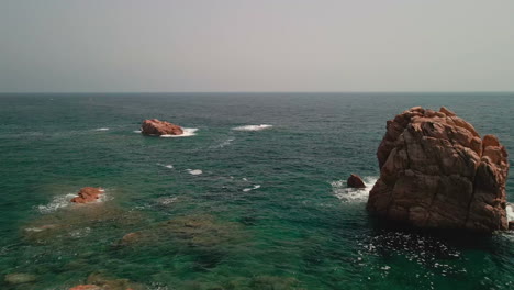 Mar-Idílico-Con-Rocas-Y-Olas-Rompientes-En-Un-Día-Soleado-De-Verano-En-Cerdeña,-Italia---Retroceso-Aéreo