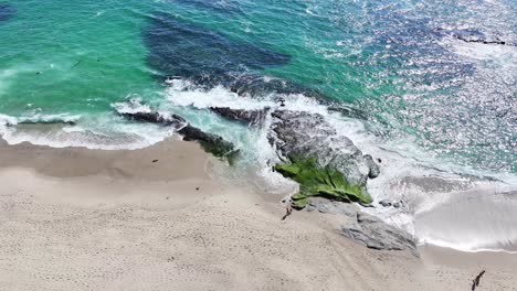 Rotación-Alrededor-De-Un-Afloramiento-Rocoso-En-La-Playa-De-Aliso-En-El-Sur-De-California-Durante-El-Día-El-Sol-Brillante-Y-La-Gente-Caminando-Por-La-Playa-60fps