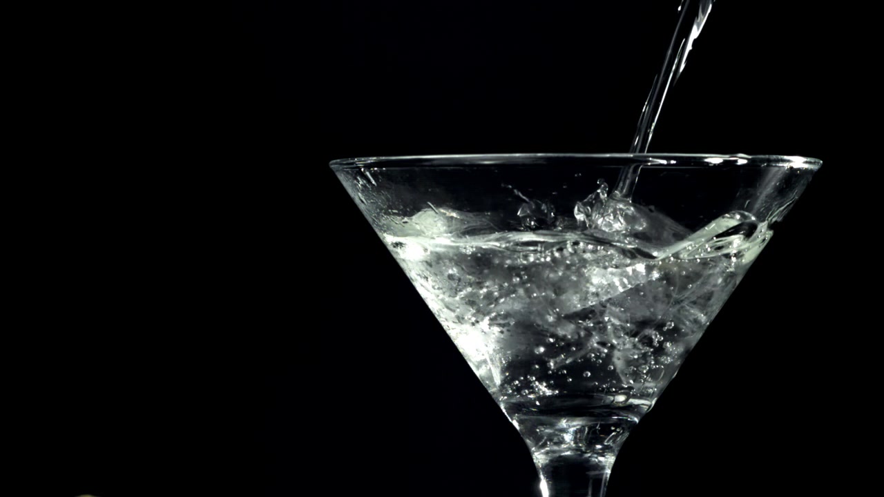 Versamento di acqua al rallentatore in un bicchiere da Martini con ghiaccio