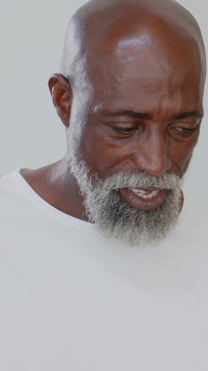 Vertical video: Reading paper below, man replying offscreen, turning right at home in white shirt