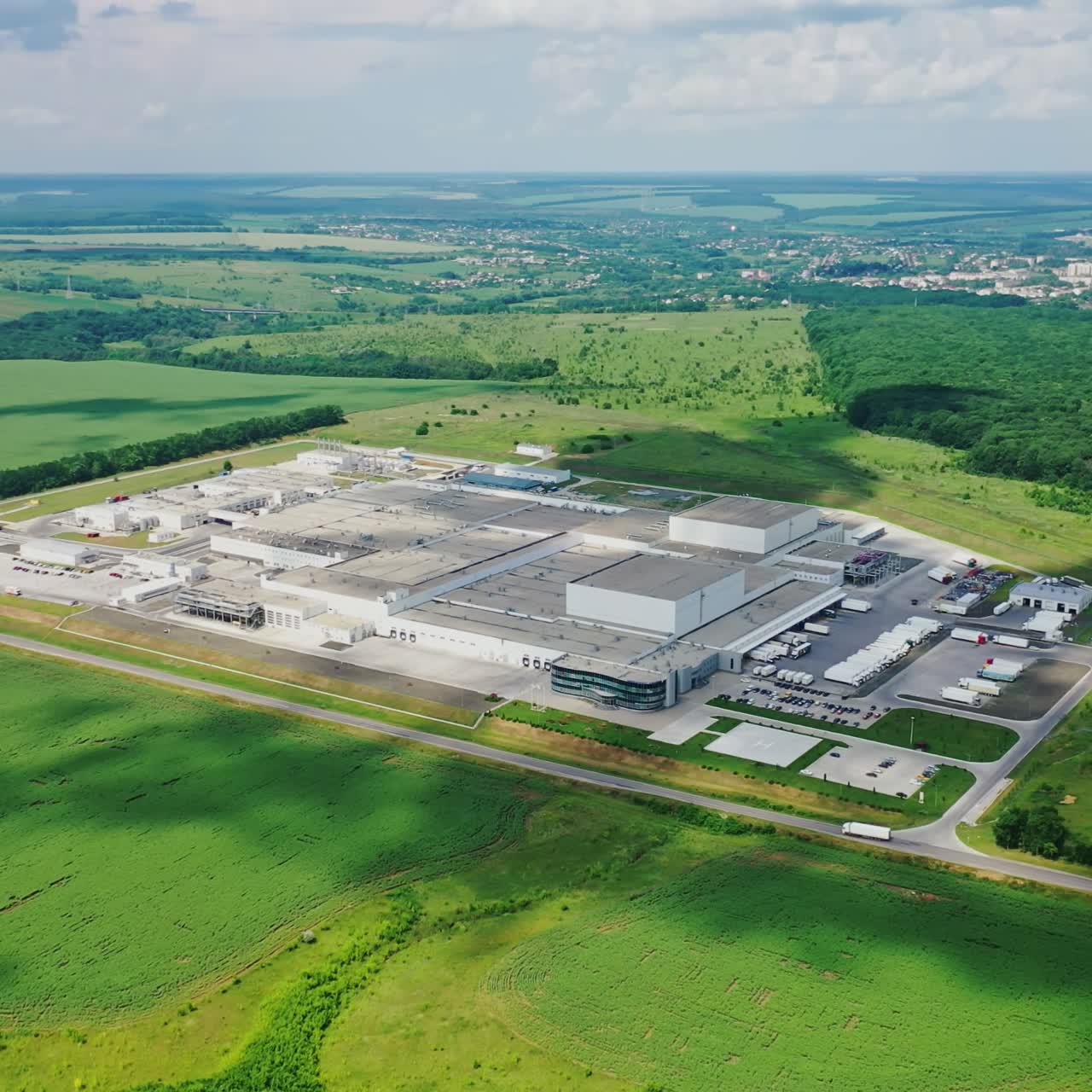 Large plant surrounded by green nature. Manufacturing in the countryside in summer. Modern industrial complex on field. Aerial view.